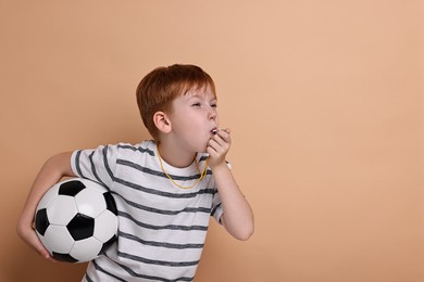 Little boy with soccer ball blowing whistle on beige background, space for text