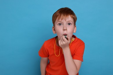 Little boy blowing whistle on light blue background