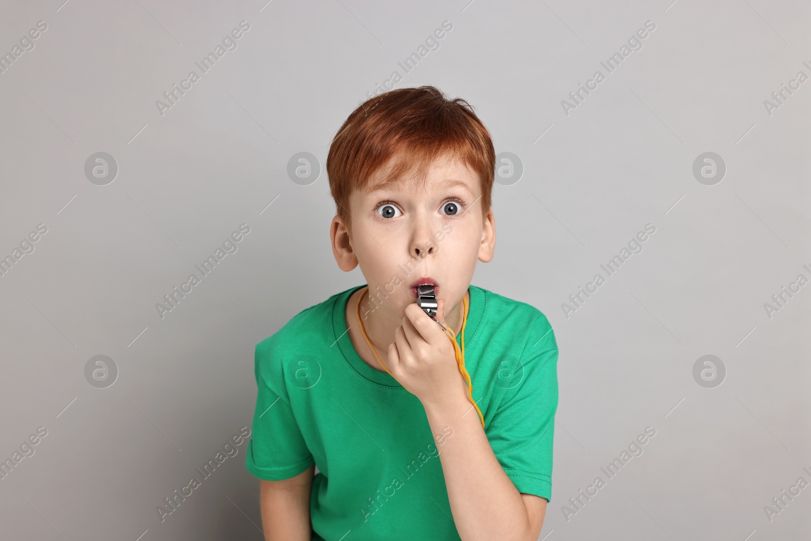 Photo of Little boy blowing whistle on grey background