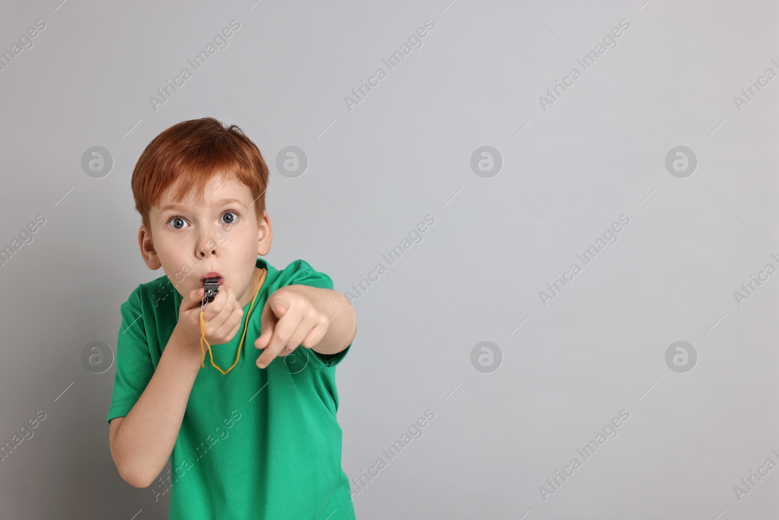 Photo of Little boy blowing whistle on grey background, space for text