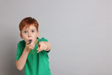 Photo of Little boy blowing whistle on grey background, space for text