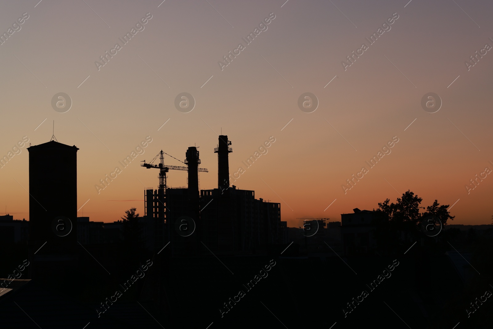 Photo of Buildings, tower crane and trees under beautiful sky in evening