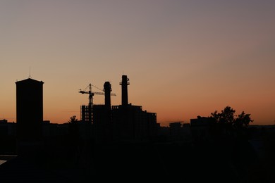 Buildings, tower crane and trees under beautiful sky in evening