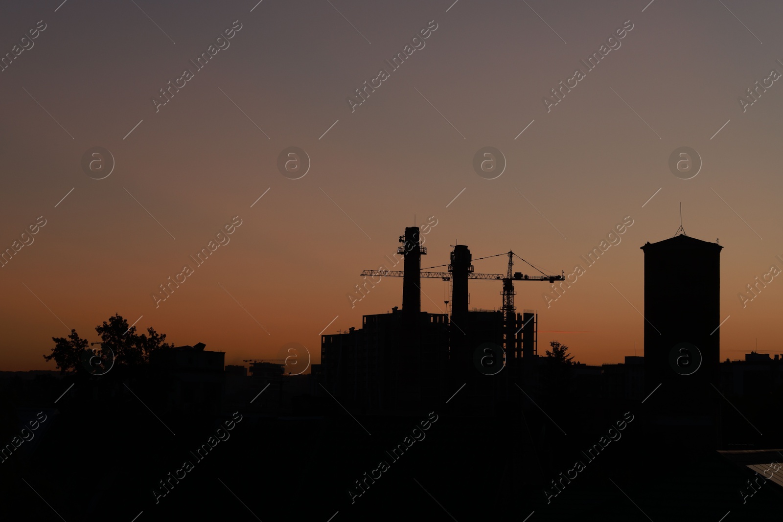 Photo of Buildings, tower crane and trees under beautiful sky in evening