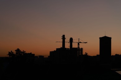 Buildings, tower crane and trees under beautiful sky in evening