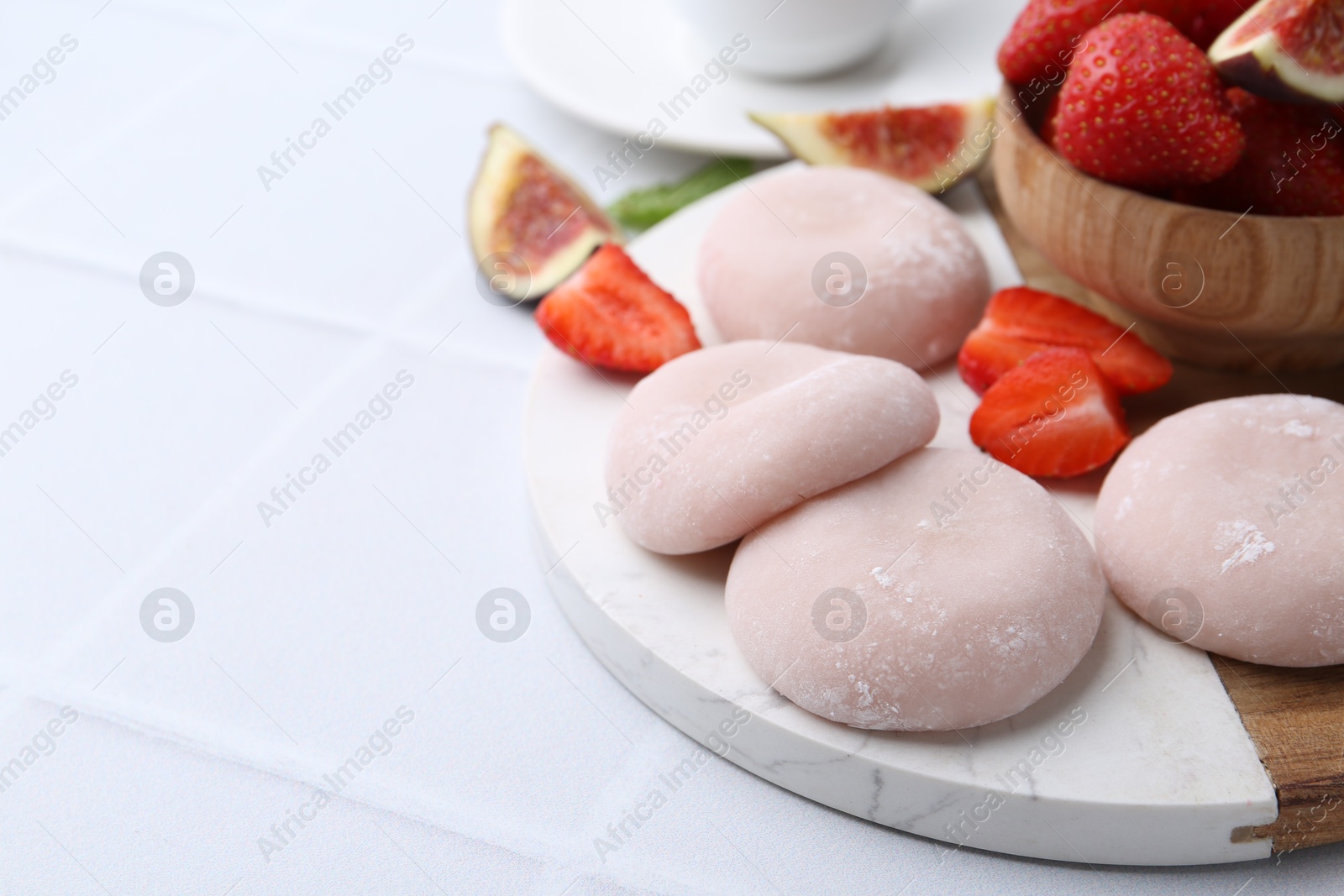 Photo of Delicious mochi, strawberries and fig on white tiled table, closeup. Space for text