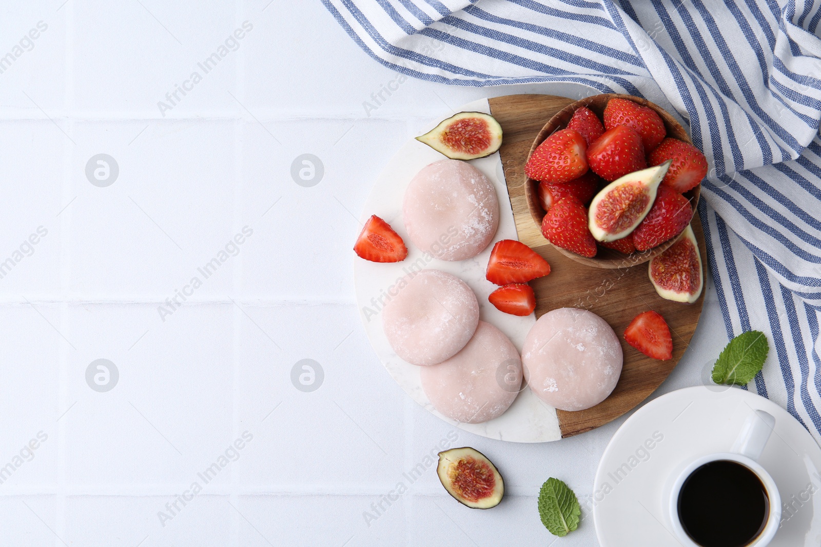 Photo of Delicious mochi, strawberries, figs and coffee on white tiled table, top view. Space for text