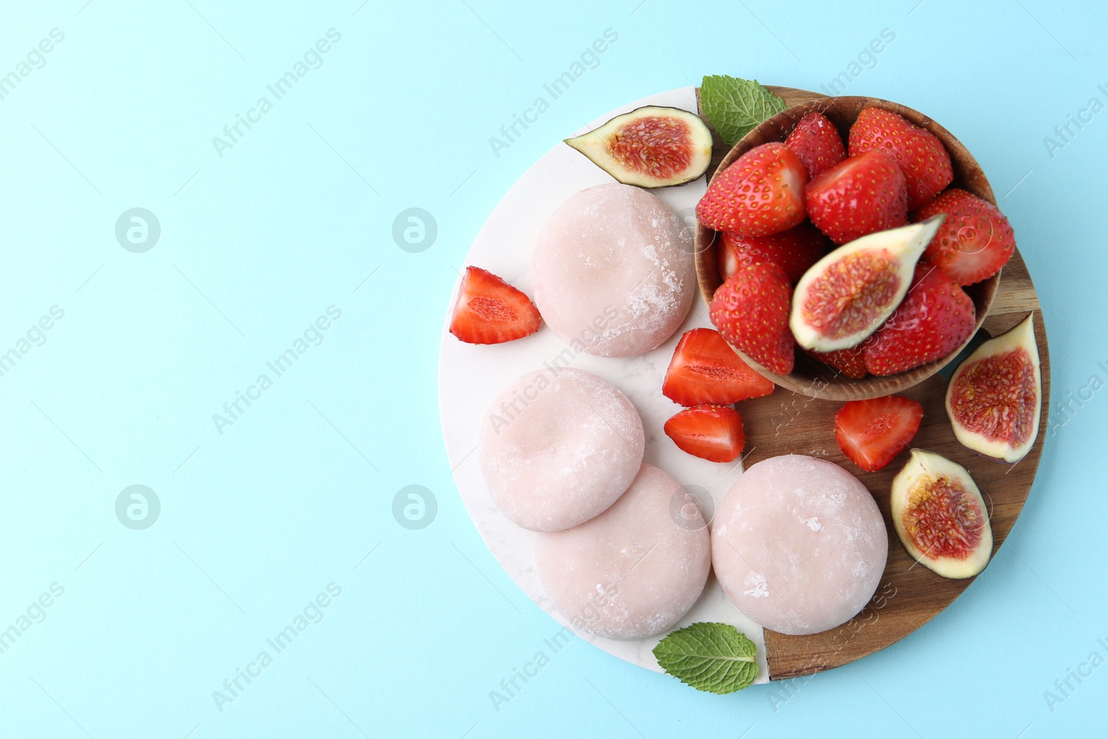 Photo of Delicious mochi, strawberries and figs on light blue background, top view. Space for text