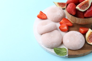 Photo of Delicious mochi, strawberries and figs on light blue background, closeup. Space for text