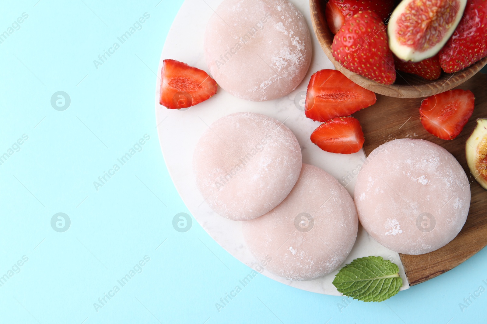 Photo of Delicious mochi, strawberries and fig on light blue background, top view