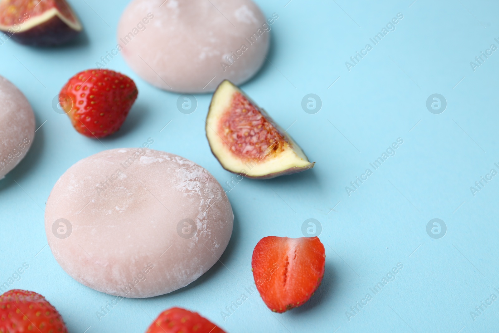 Photo of Delicious mochi, strawberries and figs on light blue background, closeup. Space for text