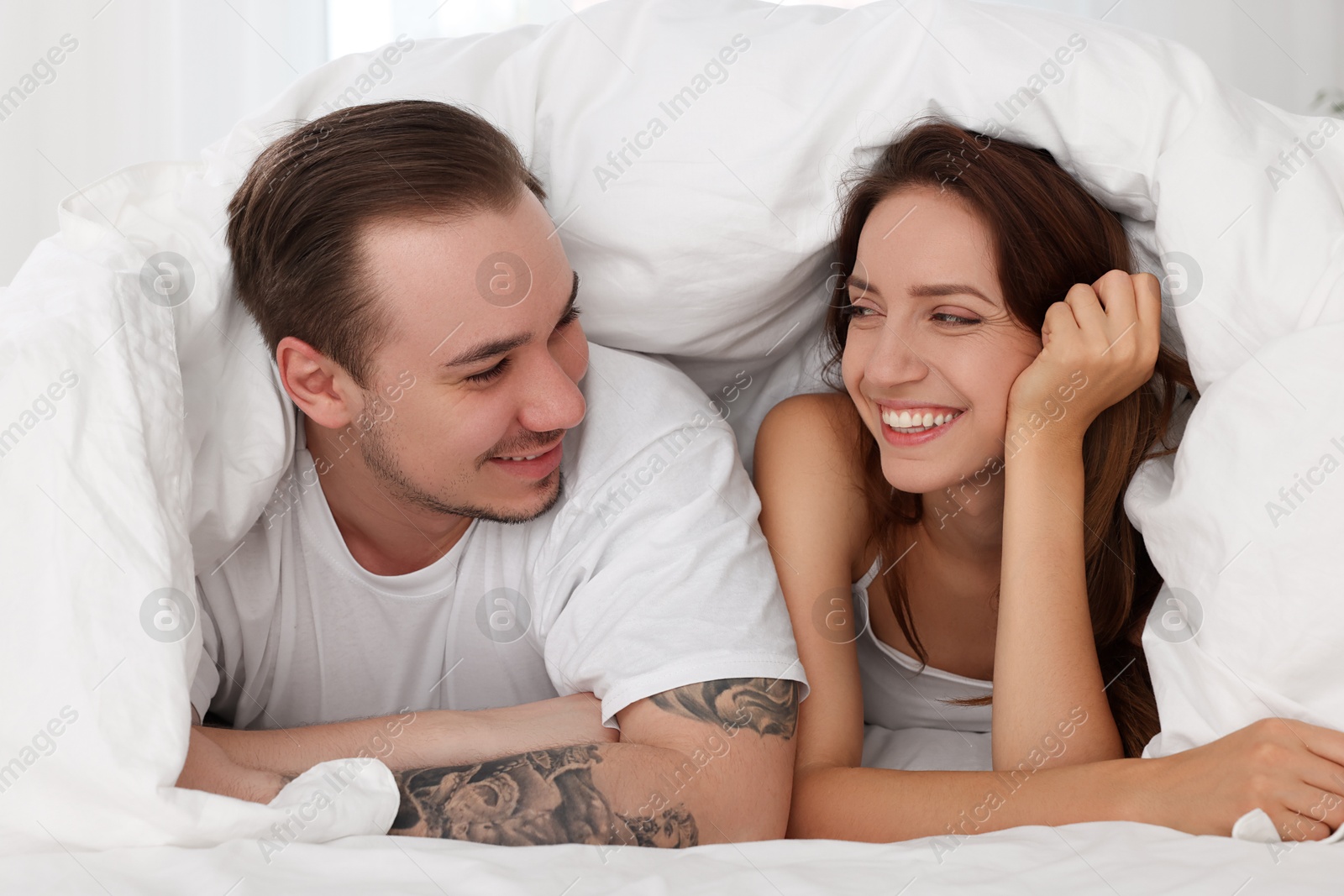 Photo of Happy couple spending time together wrapping in duvet in bed at home