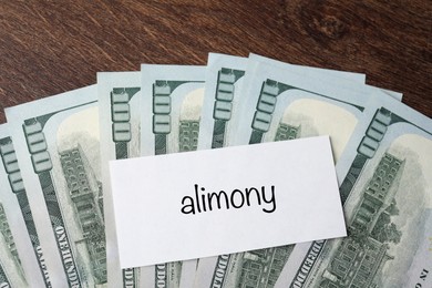 Photo of Alimony. Blank card and dollar banknotes on wooden table, top view