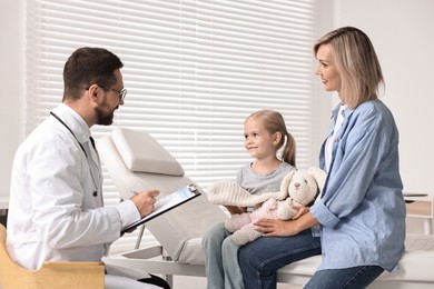 Photo of Doctor consulting little girl with toy and her mother in hospital