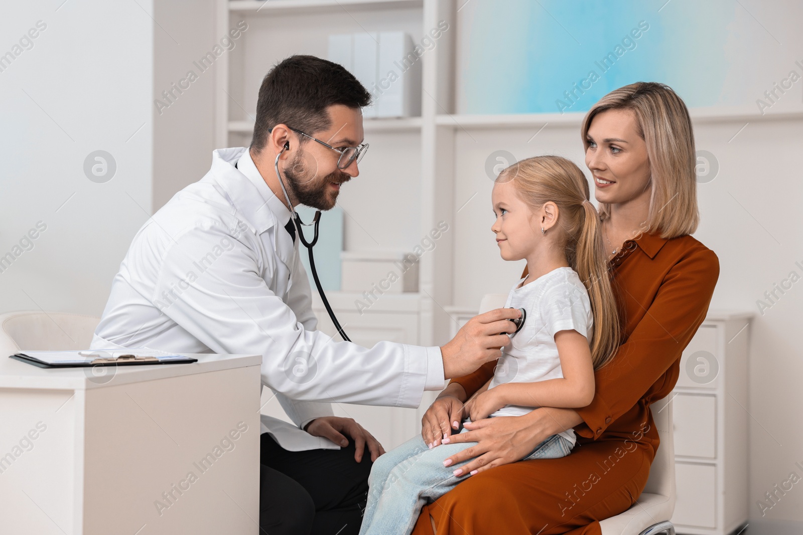 Photo of Doctor examining little girl with stethoscope and her mother in hospital