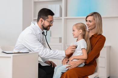 Doctor examining little girl with stethoscope and her mother in hospital