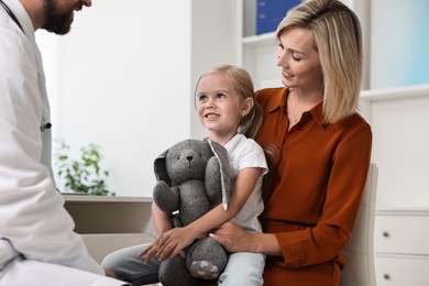 Doctor consulting little girl with toy and her mother in hospital, closeup