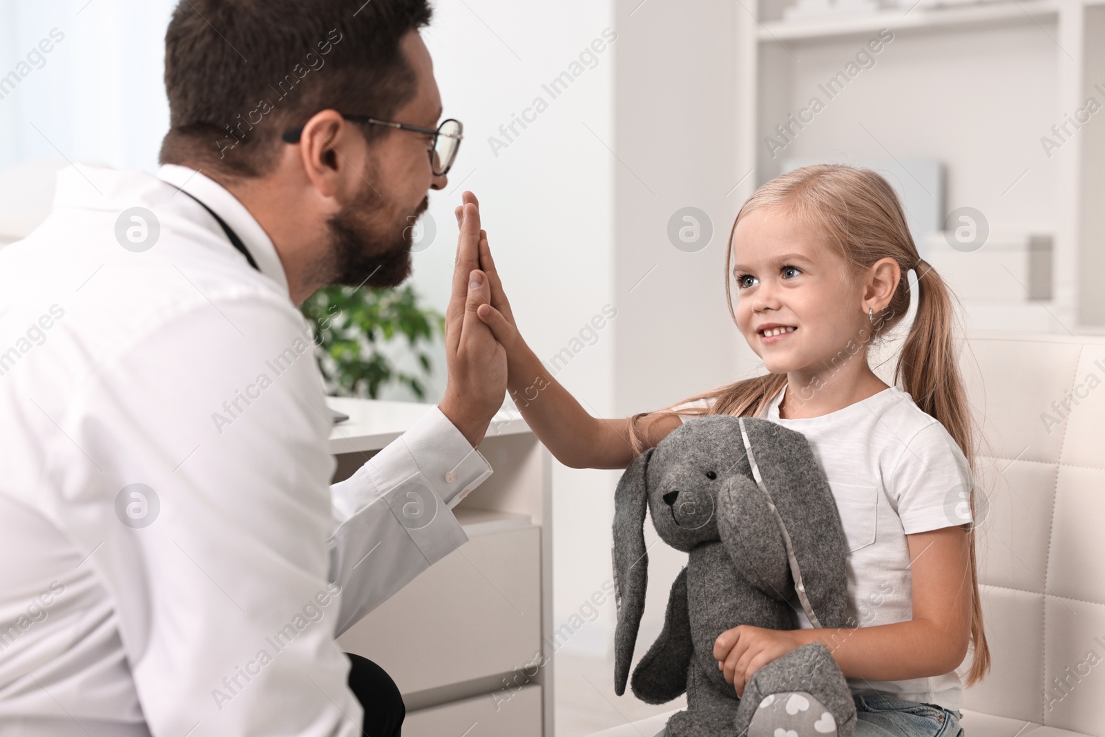 Photo of Doctor giving high five to little girl with toy in hospital