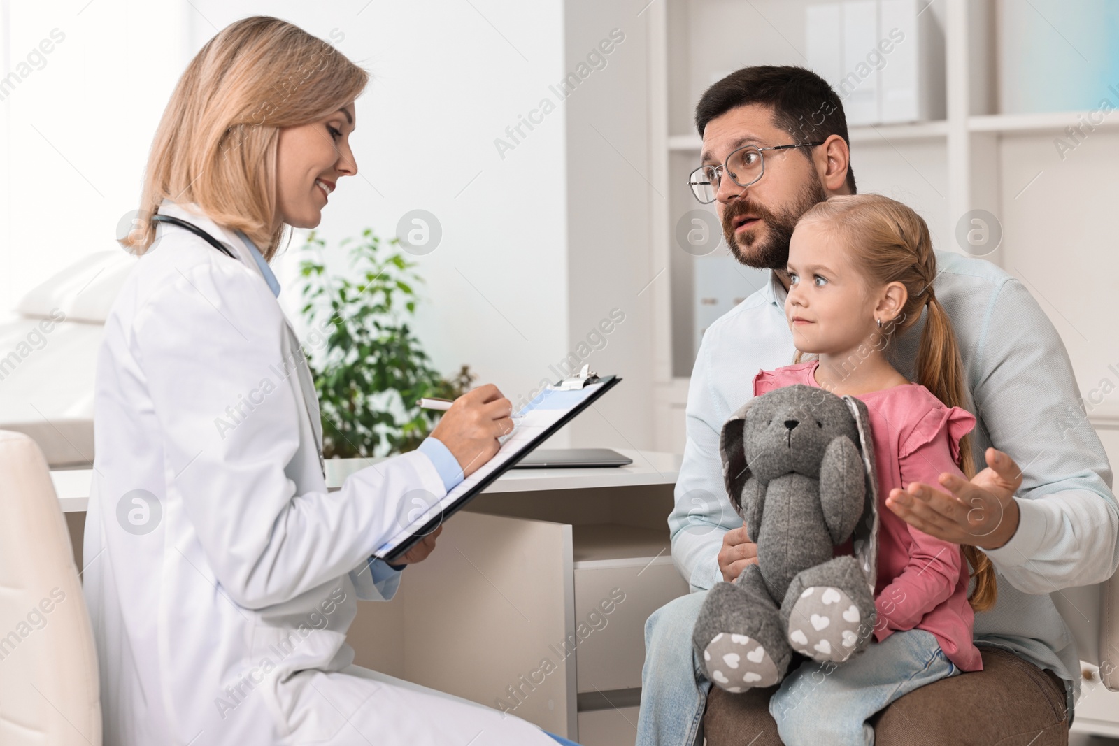 Photo of Doctor consulting little girl with toy and her father in hospital