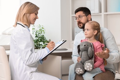 Doctor consulting little girl with toy and her father in hospital