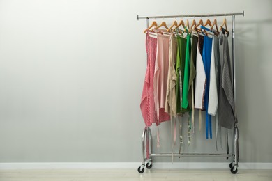 Many chef's aprons on clothing rack near light grey wall, space for text