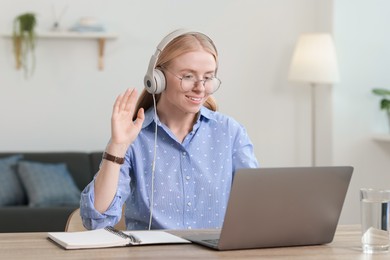 Photo of Interpreter in headphones having video chat via laptop at table indoors