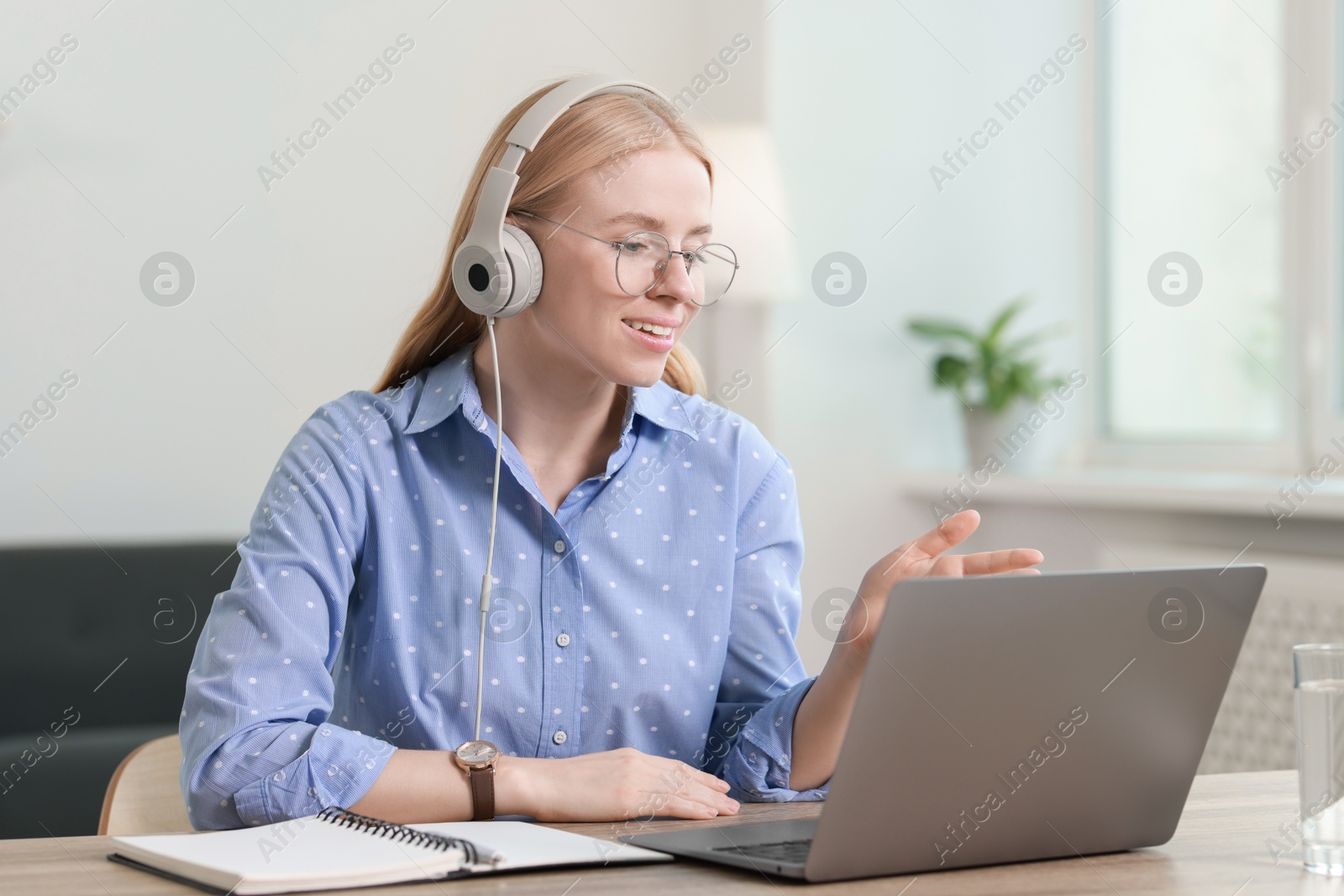 Photo of Interpreter in headphones having video chat via laptop at table indoors