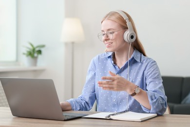 Photo of Interpreter in headphones having video chat via laptop at table indoors