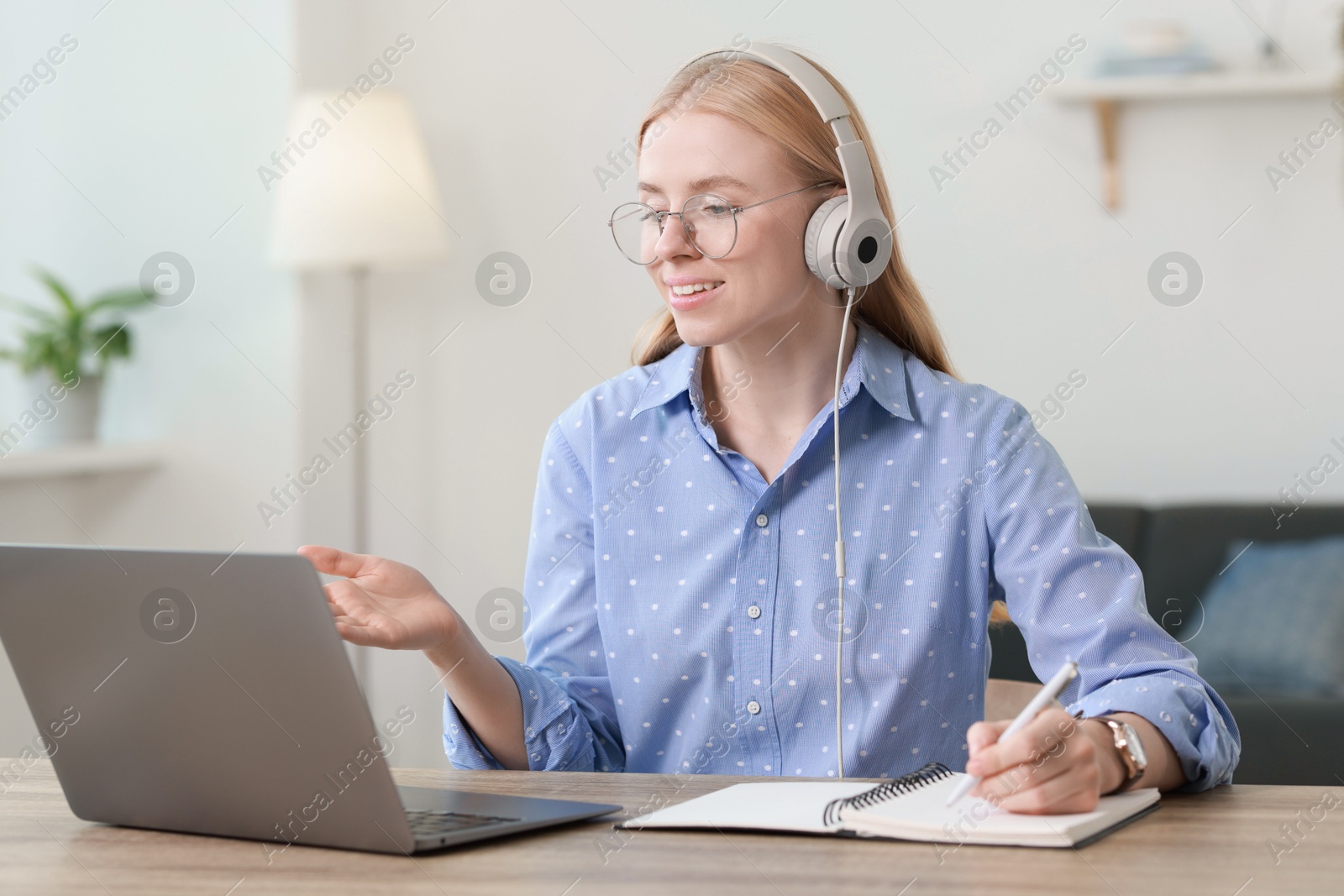 Photo of Interpreter in headphones taking notes while having video chat via laptop at table indoors