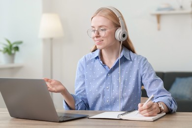 Interpreter in headphones taking notes while having video chat via laptop at table indoors