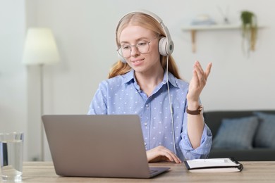 Photo of Interpreter in headphones having video chat via laptop at table indoors