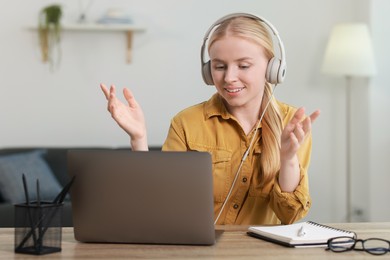 Interpreter in headphones having video chat via laptop at table indoors