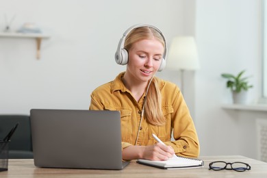 Interpreter in headphones taking notes while working with laptop at table indoors