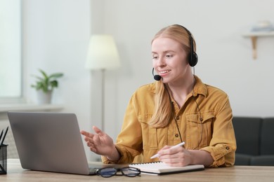 Photo of Interpreter in headset taking notes while having video chat via laptop at table indoors