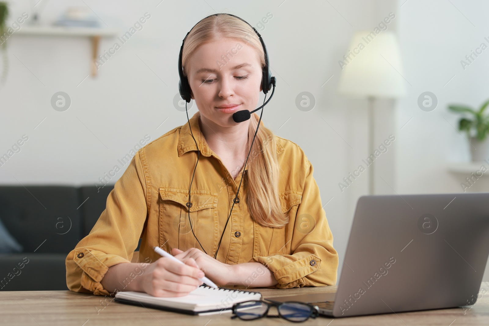 Photo of Interpreter in headset taking notes while working with laptop at table indoors