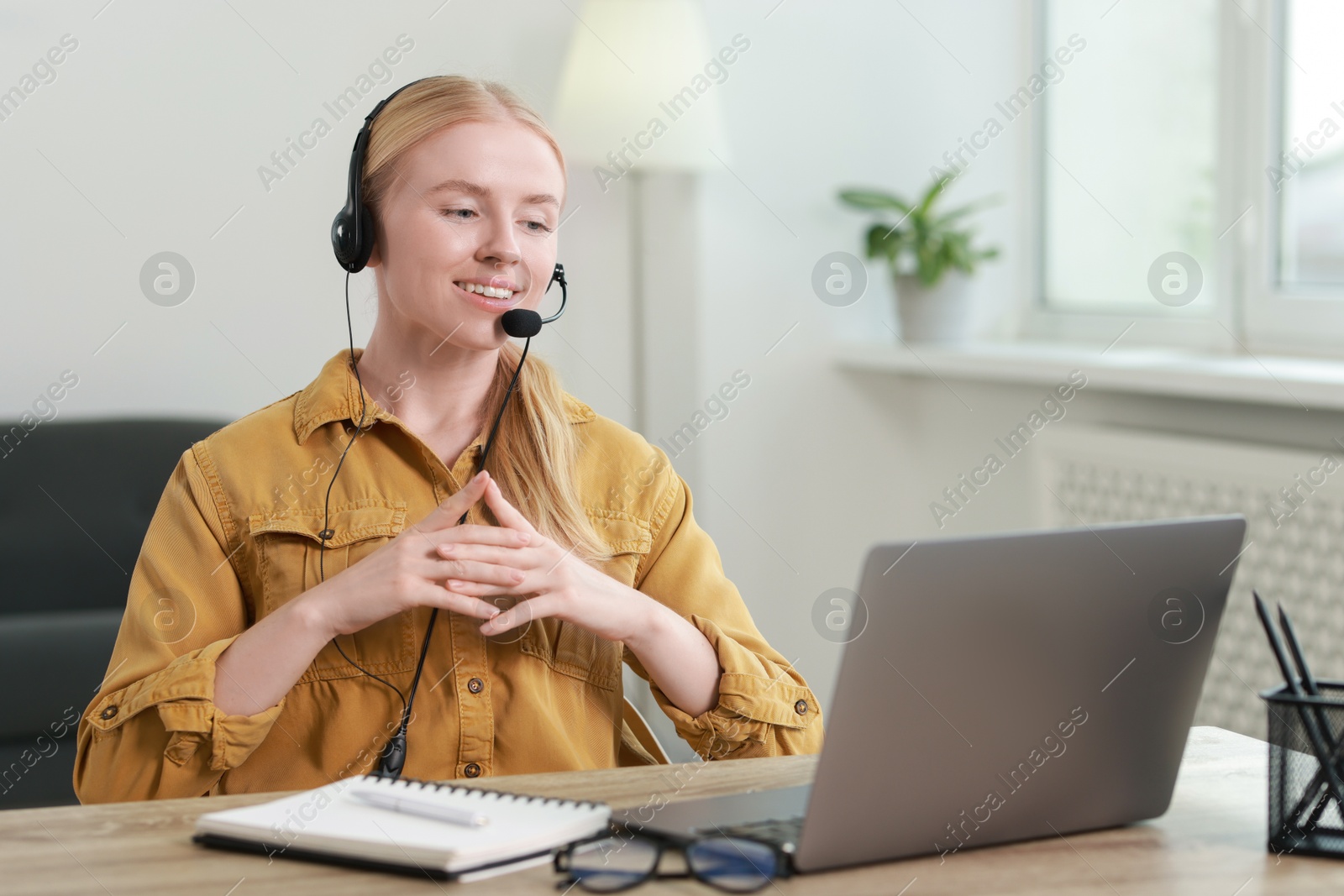 Photo of Interpreter in headset having video chat via laptop at table indoors