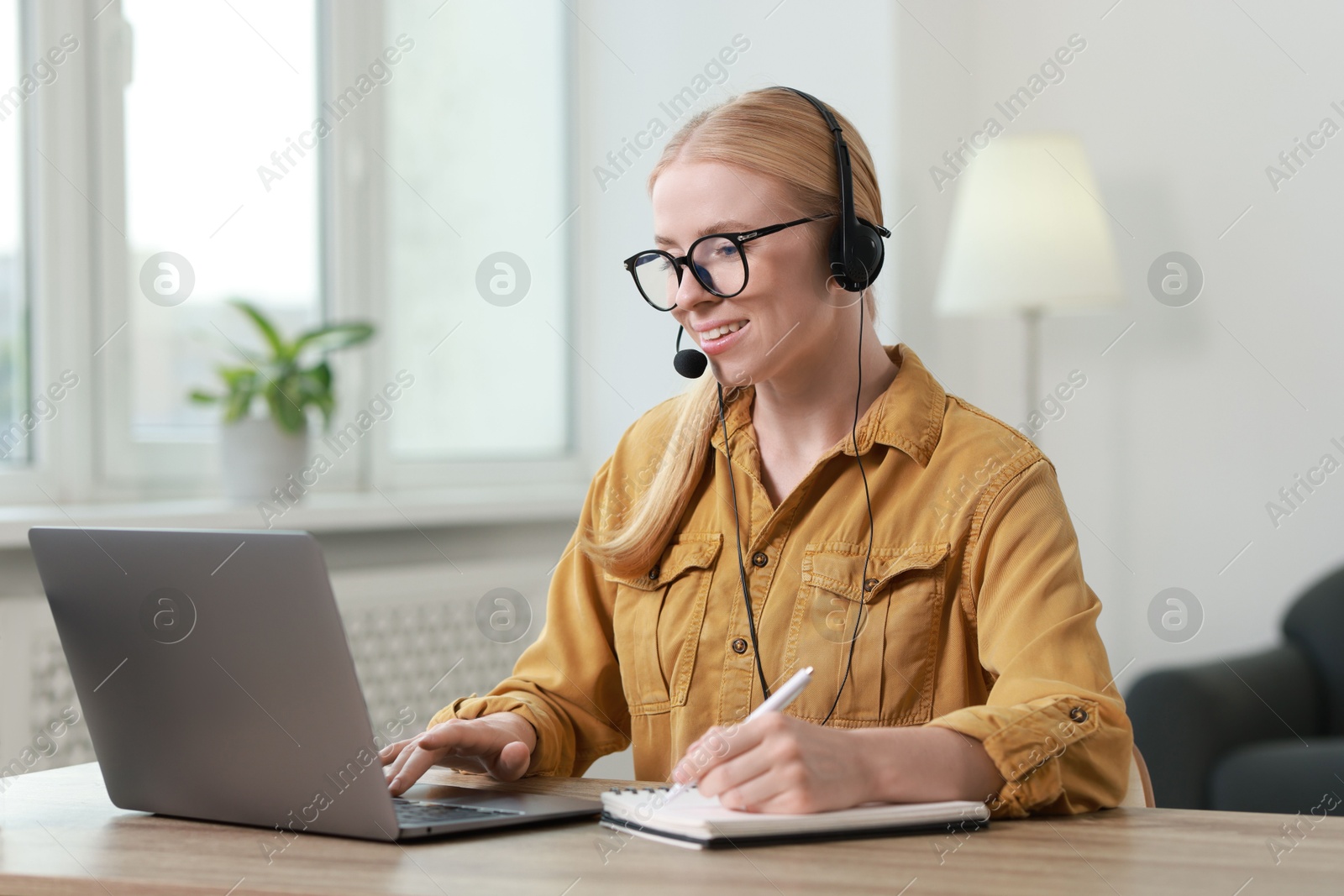 Photo of Interpreter in headset taking notes while working with laptop at table indoors