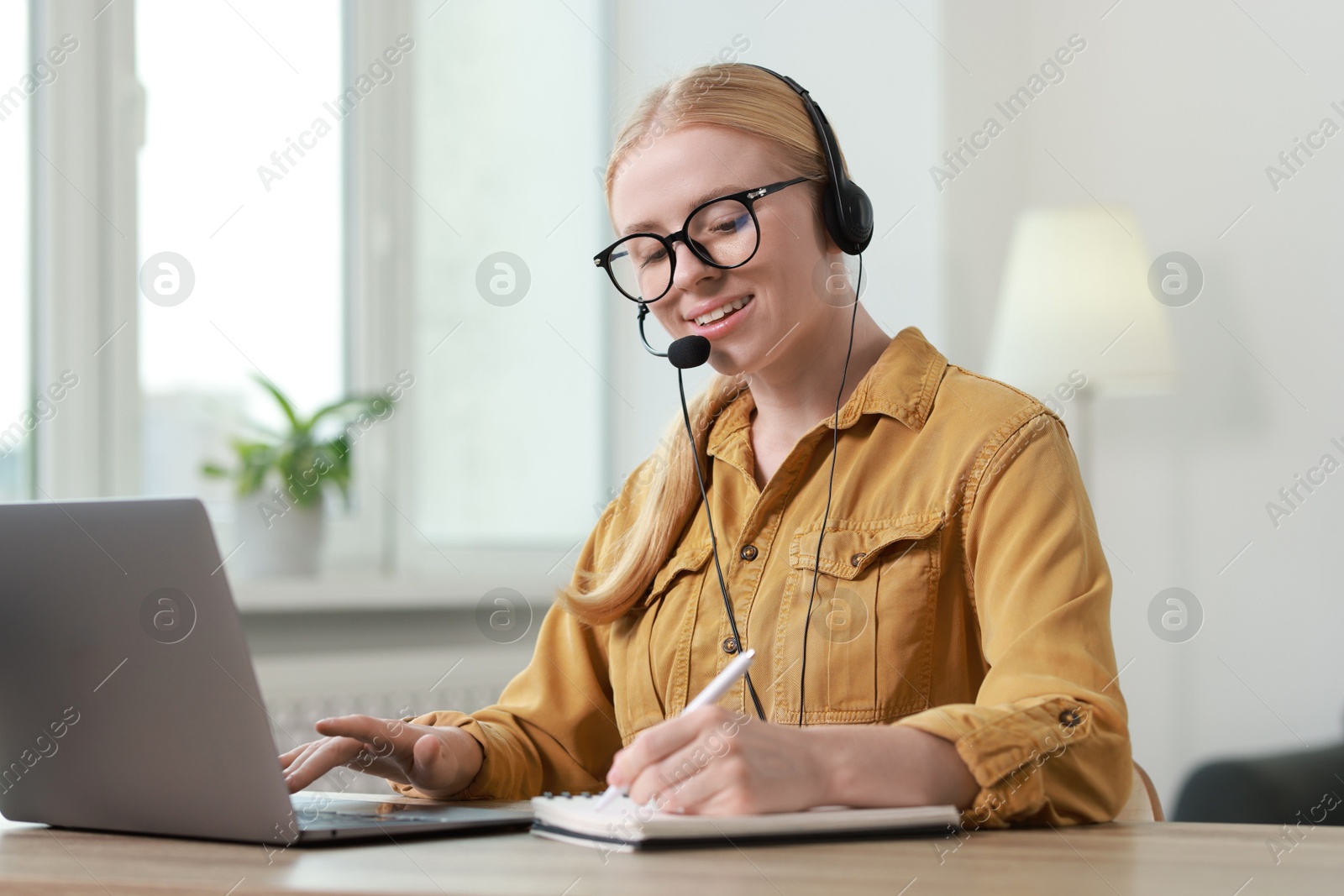 Photo of Interpreter in headset taking notes while working with laptop at table indoors