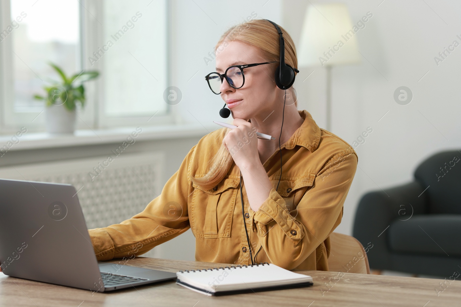 Photo of Interpreter in headset working with laptop at table indoors