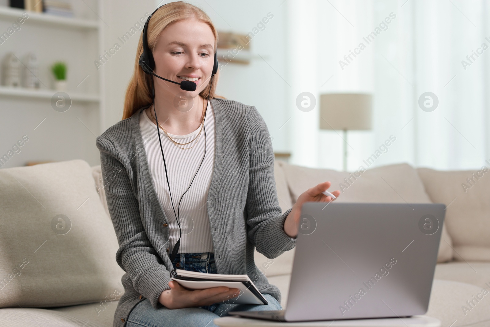 Photo of Interpreter in headset having video chat via laptop on sofa at home