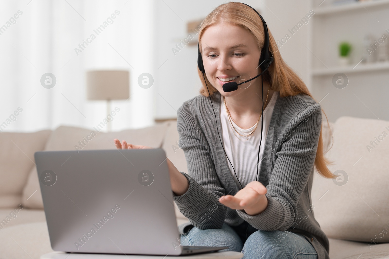 Photo of Interpreter in headset having video chat via laptop on sofa at home