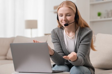 Photo of Interpreter in headset having video chat via laptop on sofa at home