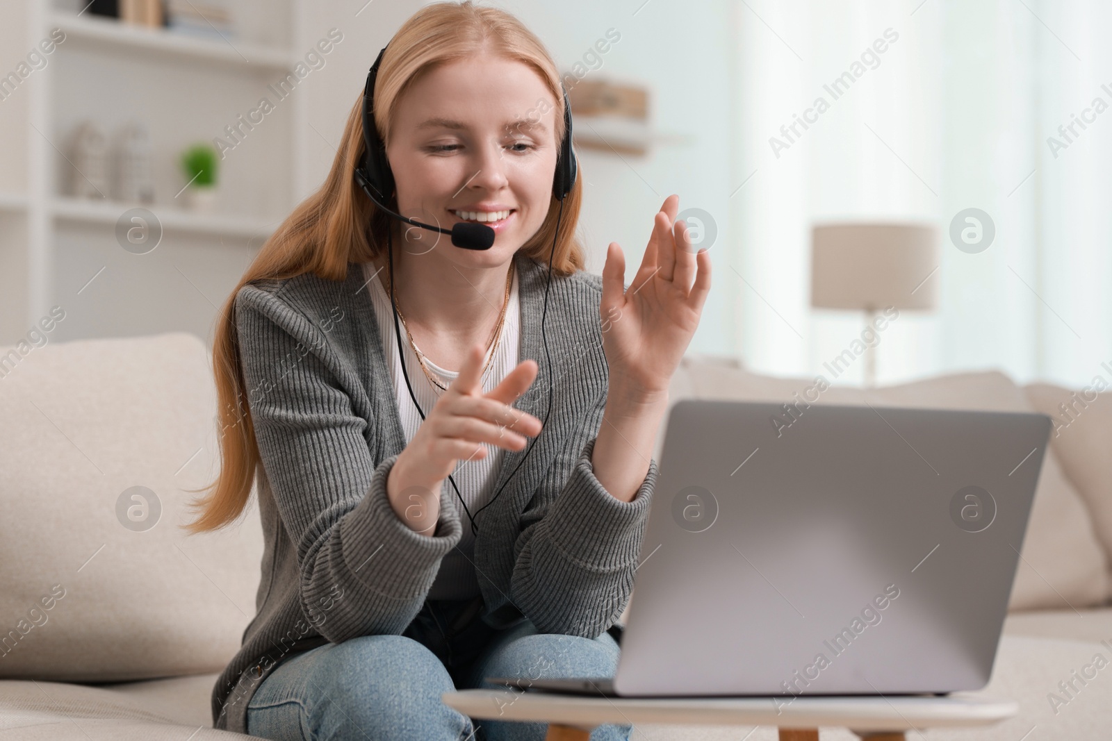 Photo of Interpreter in headset having video chat via laptop on sofa at home