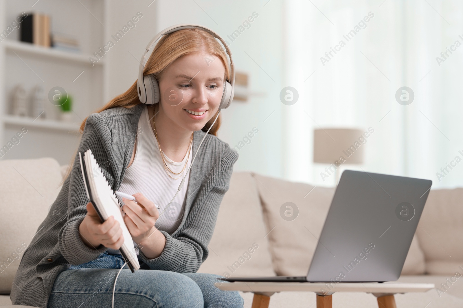 Photo of Interpreter in headphones having video chat via laptop on sofa at home