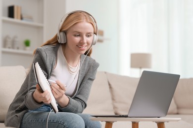 Interpreter in headphones having video chat via laptop on sofa at home