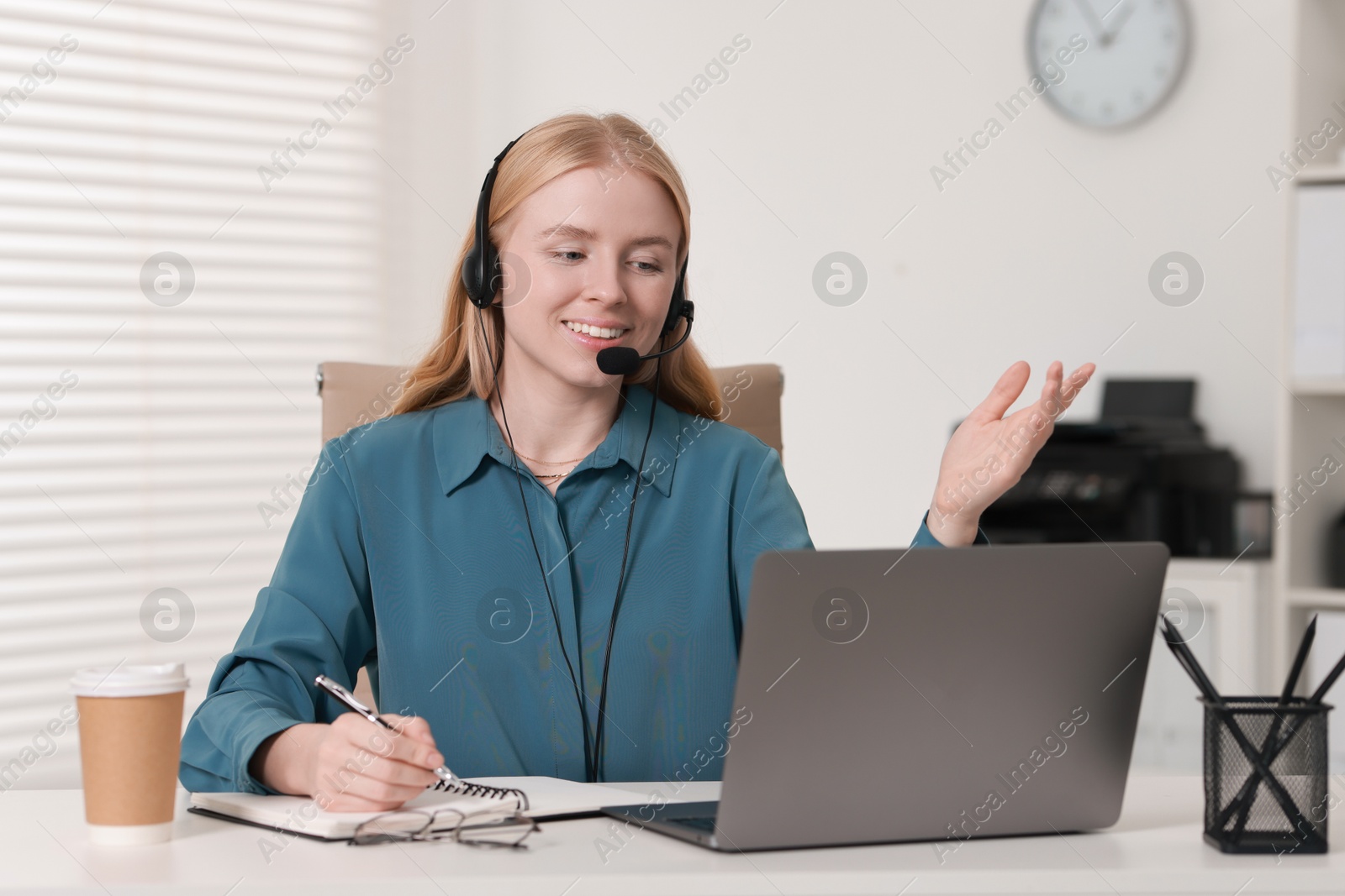 Photo of Interpreter in headset taking notes while having video chat via laptop at table indoors