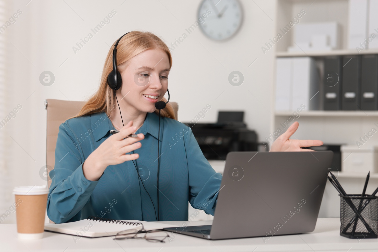 Photo of Interpreter in headset having video chat via laptop at table indoors