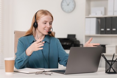 Interpreter in headset having video chat via laptop at table indoors