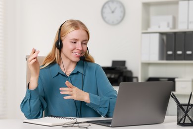 Interpreter in headset having video chat via laptop at table indoors