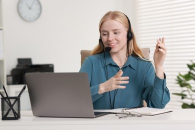 Interpreter in headset having video chat via laptop at table indoors